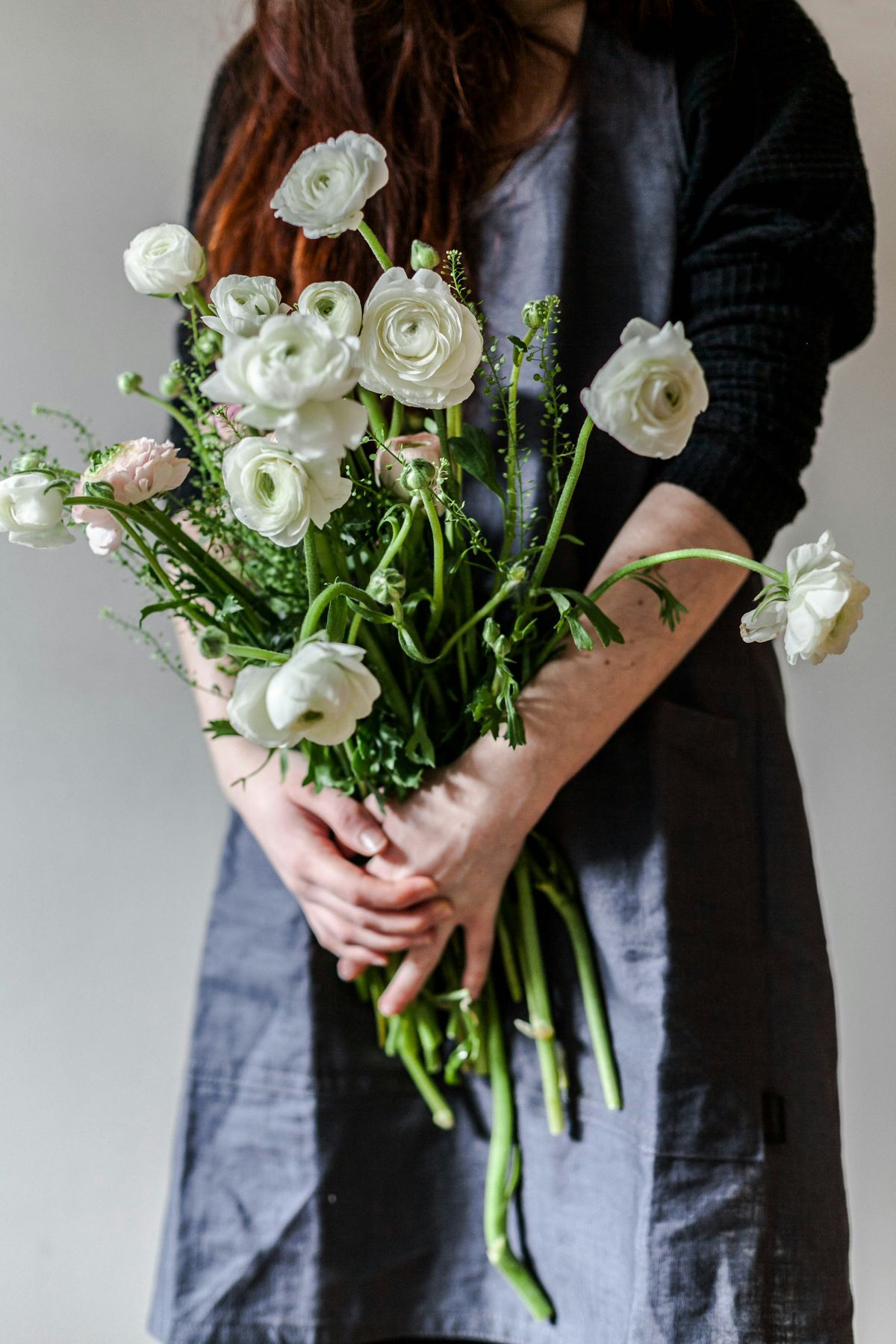 A person in a gray dress holding a bouquet of white ranunculus